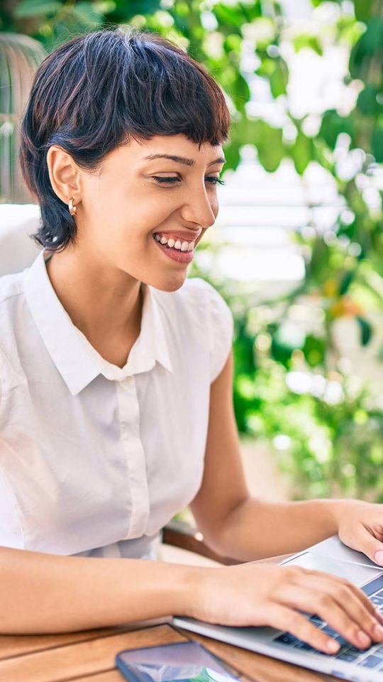 a woman is smiling while using a laptop computer at The Cedars Apartments