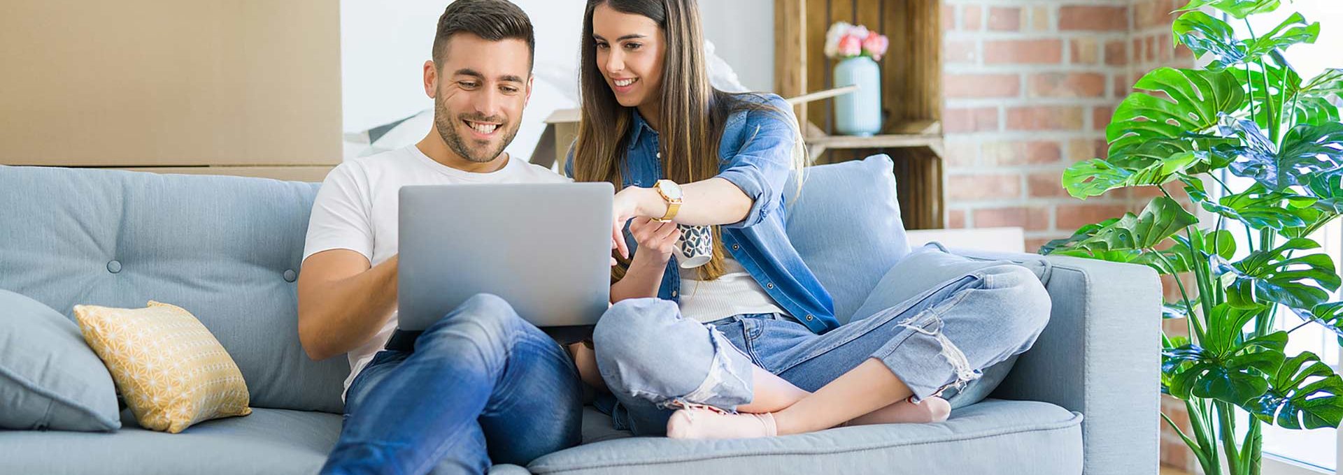 a man and woman sitting on a couch with a laptop at The Cedars Apartments