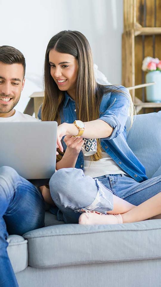 a man and woman sitting on a couch with a laptop at The Cedars Apartments