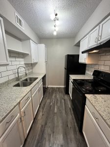 a kitchen with white cabinets and black appliances at The Cedars Apartments
