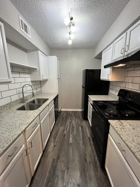 a kitchen with white cabinets and black appliances at The Cedars Apartments