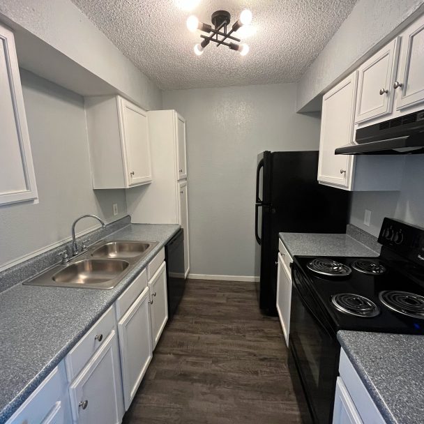 a kitchen with white cabinets and black appliances at The Cedars Apartments