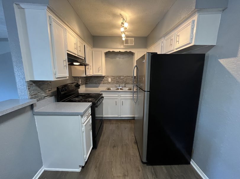 a kitchen with white cabinets and black appliances at The Cedars Apartments