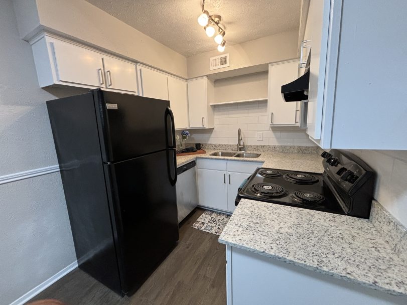 a kitchen with black appliances and white cabinets at The Cedars Apartments